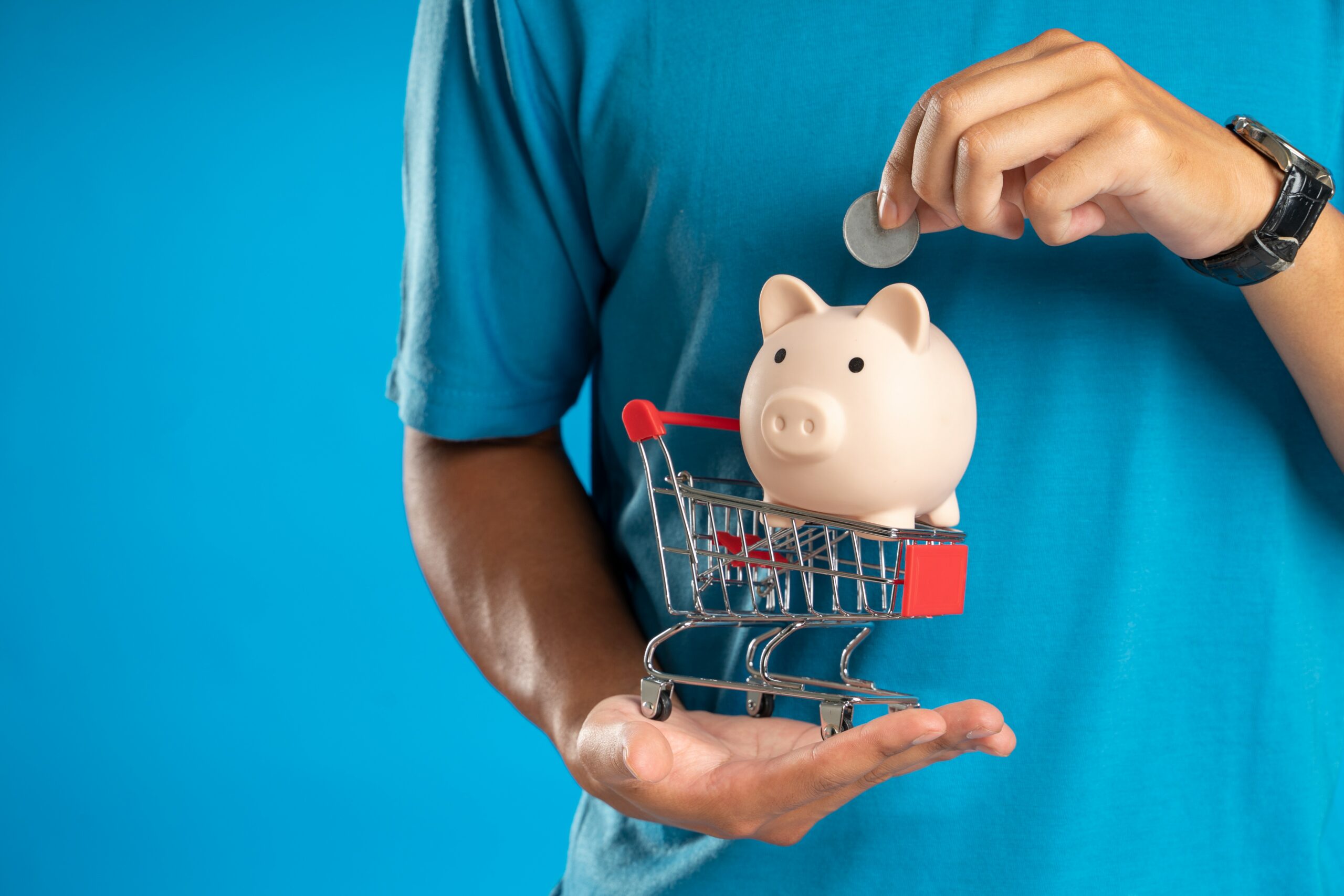 A white man holding a miniature piggy bank in a shopping trolley. 