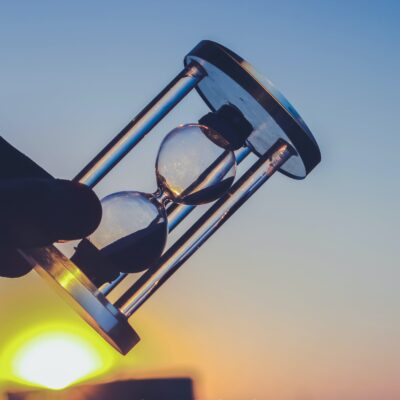 hand holding hour glass with yellow sun rising in background